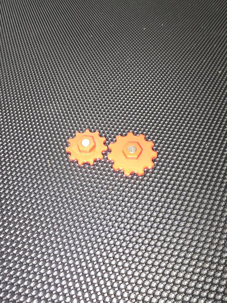 May include: Two orange plastic gears with a silver metal pin in the center of each gear.