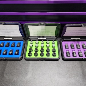 May include: Three black plastic cases with different colored inserts, each containing a set of black metal lug nuts. The cases are labeled with instructions for using the lug nuts.