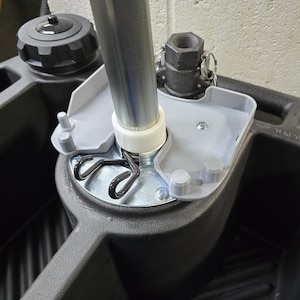 May include: Close-up of a grey plastic container with a metal pole and a grey plastic cap. The pole is attached to the container with a white plastic ring and a metal spring.