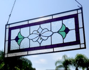May include: A stained glass window panel with a floral design. The panel is framed in black and features a white flower with green leaves and purple accents.