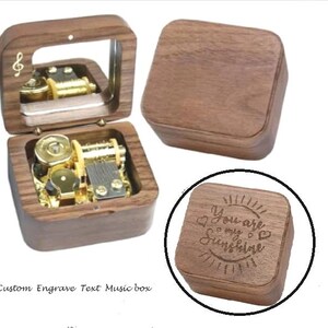 Puede incluir: Una caja de m&uacute;sica de madera con una tapa con bisagras y un espejo en el interior. La caja est&aacute; grabada con el texto "You are my sunshine" y tiene un peque&ntilde;o mecanismo de m&uacute;sica intrincado visible en el interior.
