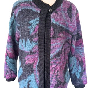 May include: A vintage cardigan sweater with a floral pattern in shades of blue, purple, and black. The sweater has a black collar, trim, and button closure. The long-sleeved sweater is made of a soft, textured material.