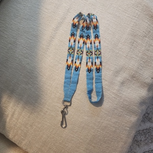 May include: A blue beaded lanyard with a silver clip. The beads are arranged in a geometric pattern with white, orange, and black accents.