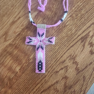 May include: A pink beaded cross necklace with black and white accents. The necklace is made of small beads and has a simple design.