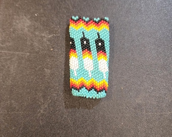 May include: A beaded rectangle with a turquoise background, black, white, red, and yellow geometric patterns.