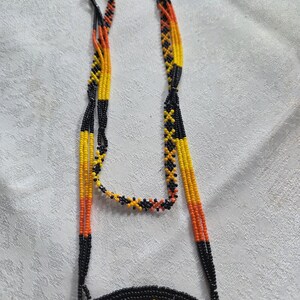 May include: A beaded necklace with a circular pendant. The necklace features strands of yellow, orange, and black beads. The pendant has a yellow background with a black border and colorful details. The necklace is likely handmade.