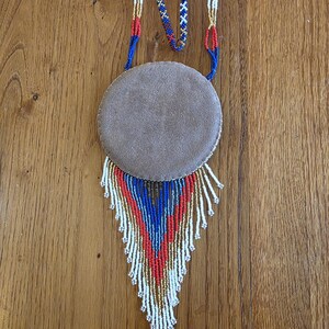 May include: A beaded necklace with a round suede pendant and a fringe of white, blue, and red beads.
