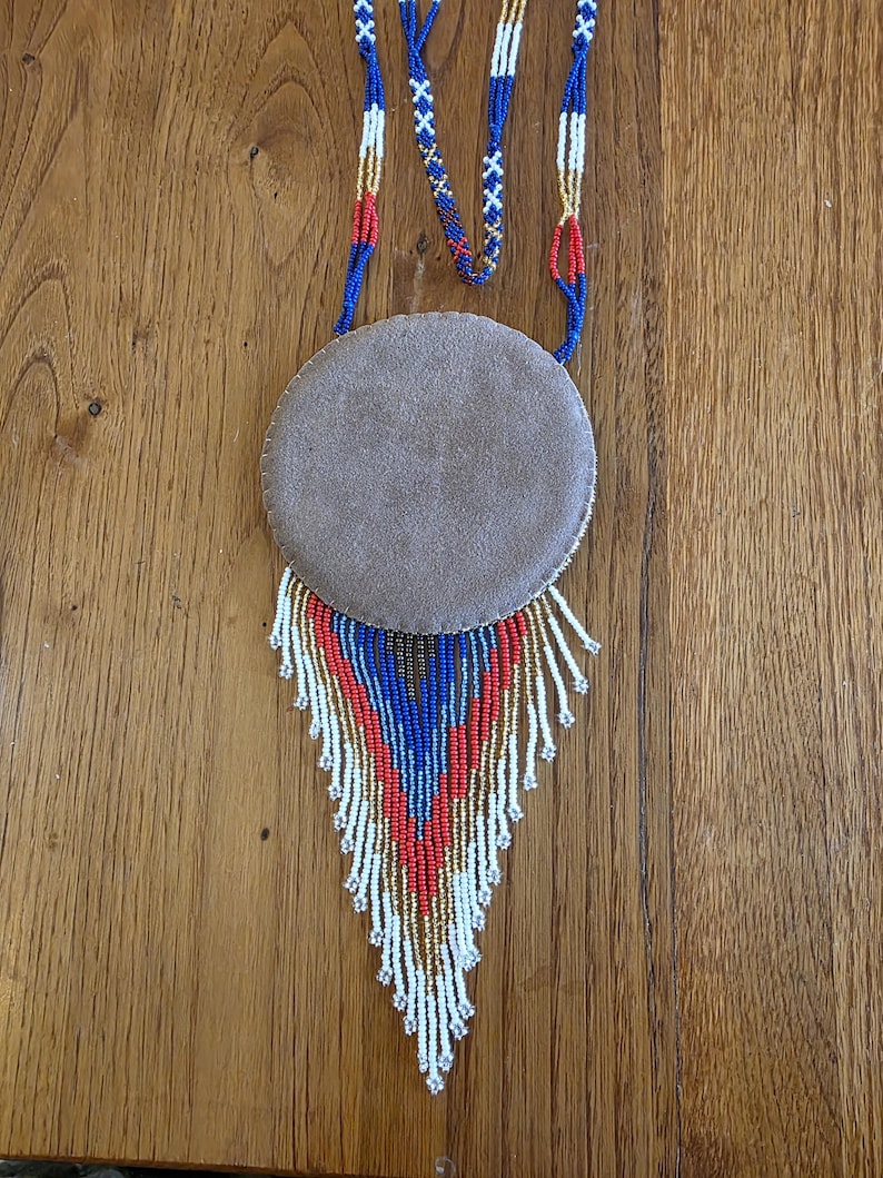 May include: A beaded necklace with a round suede pendant and a fringe of white, blue, and red beads.