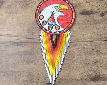 May include: A beaded Native American necklace with a red, white, and black eagle design. The necklace has a fringe of beads in orange, yellow, white, and black.