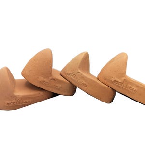 May include: Four terracotta-colored, wedge-shaped ceramic objects. Each has a curved top and a flat base. The objects are arranged in a diagonal line, with the brand name "ESCHBACH" stamped on each.