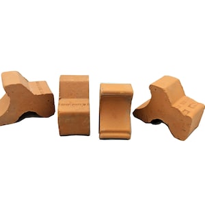 May include: Four terracotta corner pieces for a brick wall. The pieces are shaped like a triangle with a curved edge. They are a light orange color.