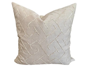 May include: A beige throw pillow with a geometric pattern embroidered in white thread.