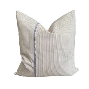 May include: A cream-colored pillow with thin black stripes and a blue and white trim down the center.