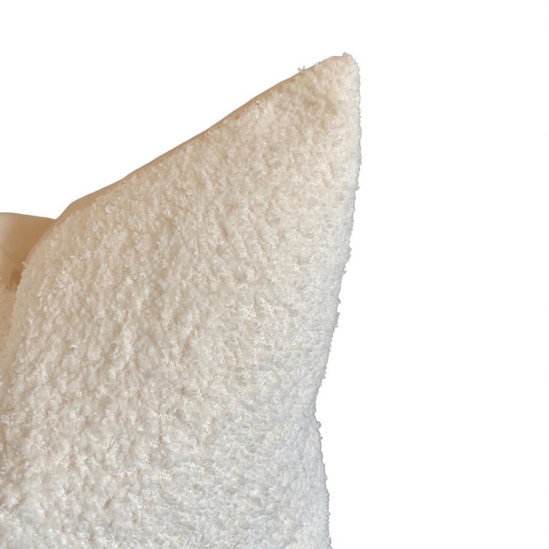 May include: A close-up of a white fluffy pillow with a soft, plush texture. The pillow is made of a fuzzy material and has a slightly pointed shape.