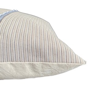 May include: A beige pillow with thin brown and white stripes. The pillow has a plain beige border.