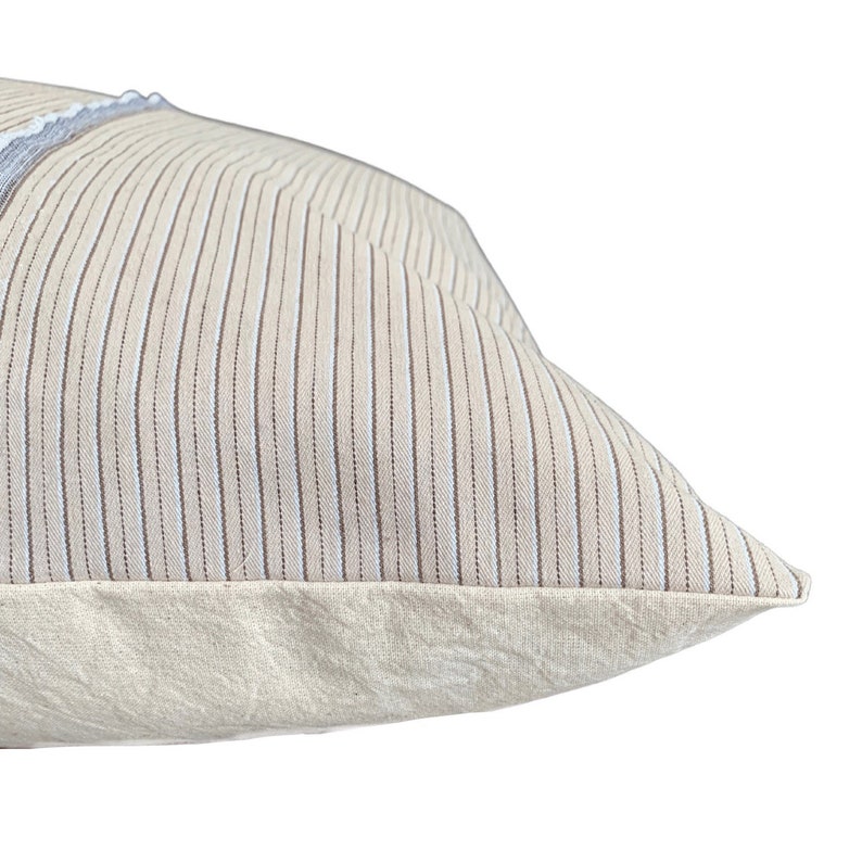 May include: A beige pillow with thin brown and white stripes. The pillow has a plain beige border.