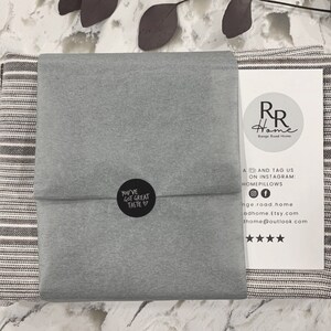 May include: A gray and white striped throw blanket is folded and wrapped in gray tissue paper. The tissue paper has a black circle sticker with the text "You've Got Great Taste" on it. The blanket is packaged with a white card with the text "RR Home" and social media information.