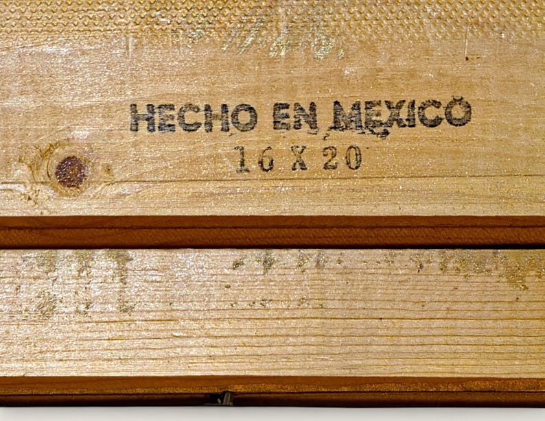 May include: Close-up of two wooden planks with the text "HECHO EN MEXICO" and "16 X 20" printed in black. The wood has a light brown color with visible grain and knots. The planks are arranged horizontally.