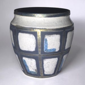 May include: A ceramic vase with a dark blue rim and a white and blue body. The body features a grid pattern with white squares and blue accents. Gold-colored lines separate the squares.