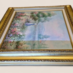 May include: An oil painting in a gold and silver ornate frame. The artwork depicts a serene landscape with a figure in blue, surrounded by colorful flowers and trees. The frame adds a touch of elegance.