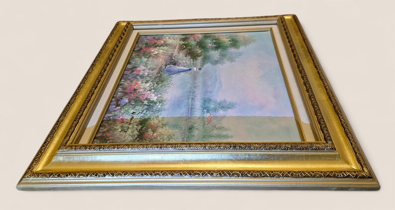 May include: An oil painting in a gold and silver ornate frame. The artwork depicts a serene landscape with a figure in blue, surrounded by colorful flowers and trees. The frame adds a touch of elegance.