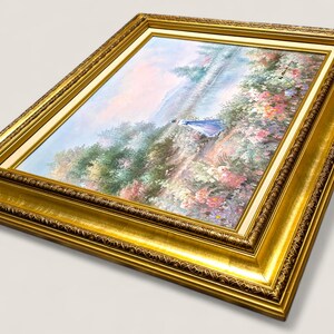 May include: A framed painting with a gold ornate frame. The artwork depicts a landscape scene with a figure in a blue dress. The painting features a variety of colors, including green, pink, and blue. The frame is a rich gold color.