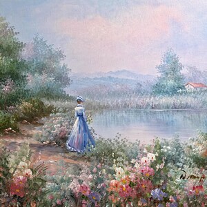 May include: Oil painting of a woman in a blue dress and hat standing near a lake. The scene is set in a garden with colorful flowers and lush greenery. A house with a red roof is visible in the distance.