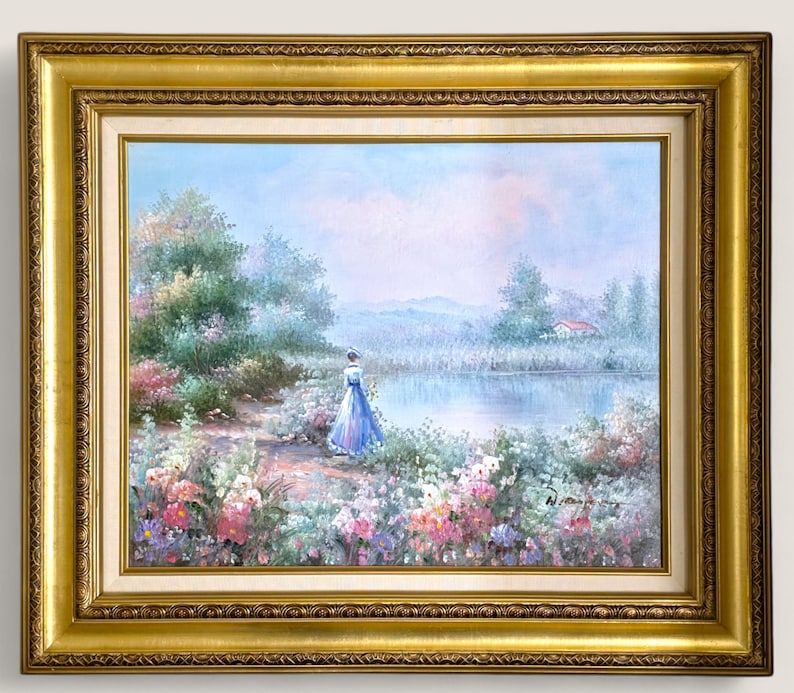 May include: A framed landscape painting featuring a woman in a blue dress near a lake. The artwork has a gold ornate frame and depicts a serene outdoor scene with colorful flowers and trees.