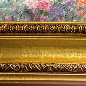 May include: Close-up of a framed floral painting. The frame is gold with intricate, dark brown decorative elements. The painting features a colorful array of pink, purple, and orange flowers.