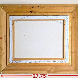 May include: Back of a framed painting. The wooden frame is rectangular, measuring 27.75 inches wide and 23.75 inches tall. The canvas is white, and the frame is a light brown color. The canvas is secured to the frame with staples.