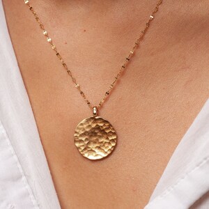 May include: A gold necklace with a hammered round pendant. The pendant is a simple circle with a textured surface.