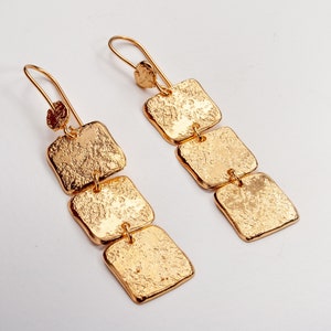 May include: Gold-tone earrings with a textured finish. Each earring features three square-shaped charms that are connected together.