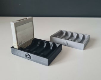 May include: Two 3D printed game cartridge holders, one black and one gray. The black holder has a Nintendo GameCube cartridge in it. Both holders have a small "C" logo on the bottom.