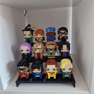 Puede incluir: Una colecci&oacute;n de 12 minifiguras Lego de personajes de la serie Harry Potter. Las figuras se muestran en un estante negro con un fondo blanco. Las figuras son de diferentes colores y tienen diferentes expresiones en sus caras.