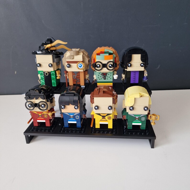 Puede incluir: Un conjunto de ocho minifiguras Lego de personajes de la serie Harry Potter. Las figuras llevan todas atuendos diferentes y tienen diferentes expresiones faciales. Las figuras est&aacute;n dispuestas en fila en un estante negro.
