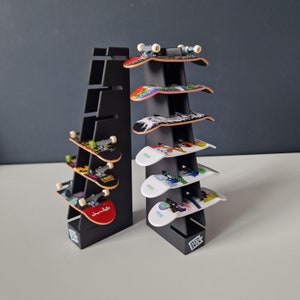 May include: Black fingerboard display stand with six fingerboards. The fingerboards have various colourful designs and graphics. The stand has a black base and a black metal frame.