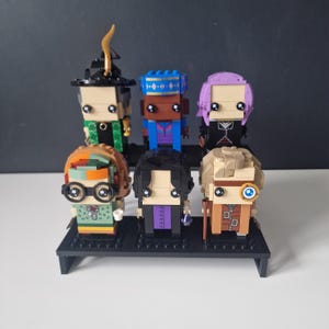 Puede incluir: Un conjunto de seis minifiguras, cada una con un dise&ntilde;o y una combinaci&oacute;n de colores &uacute;nicos. Las minifiguras se muestran en un soporte negro. Las minifiguras est&aacute;n hechas de pl&aacute;stico y tienen una variedad de expresiones faciales.
