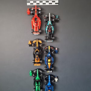 May include: A collection of six miniature racing cars, each with a different colour scheme and branding. The cars are arranged vertically, with the red car at the top and the blue car at the bottom. The cars are all made of plastic and have a realistic design.