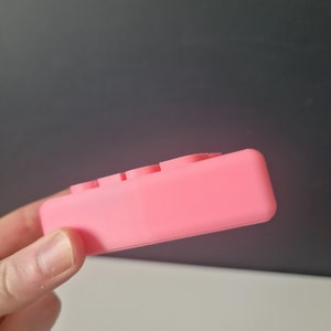 May include: A pink silicone fidget toy with four buttons. The toy is designed to help relieve stress and anxiety.