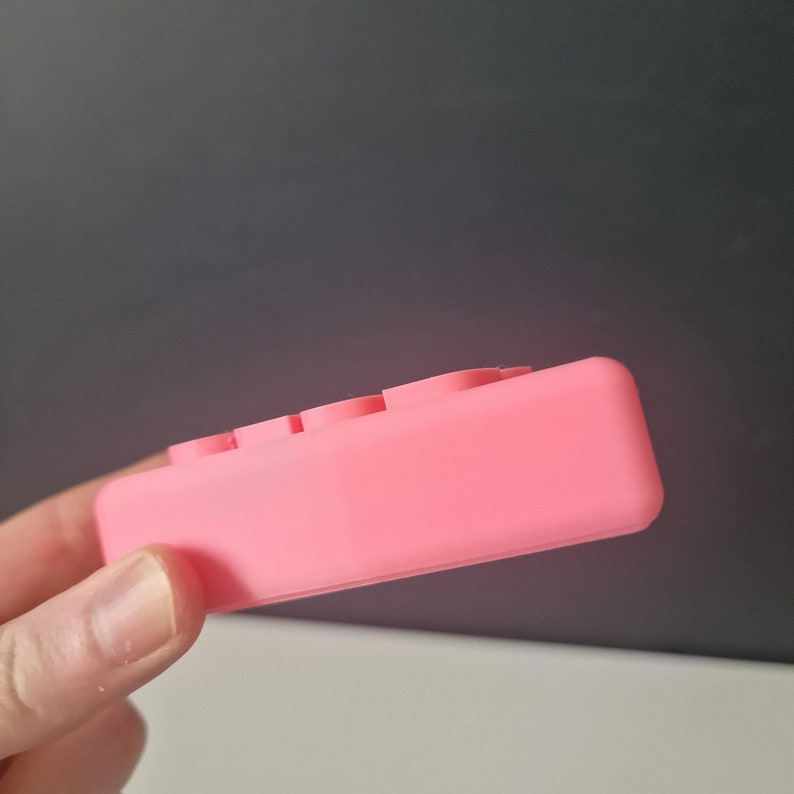 May include: A pink silicone fidget toy with four buttons. The toy is designed to help relieve stress and anxiety.