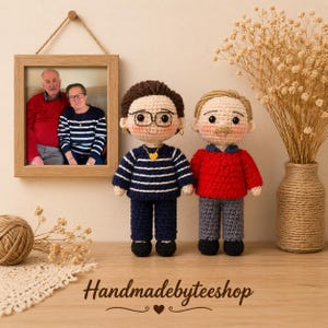 Könnte beinhalten: Zwei Häkelpuppen stehen nebeneinander. Die linke Puppe hat braune Haare, eine schwarze Brille, eine goldene Herz-Halskette, einen dunkelblau gestreiften Pullover und eine dunkelblaue Hose. Die rechte Puppe hat hellbraune Haare, einen roten Pullover und eine graue Hose.