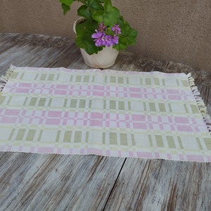 May include: A pink and green checkered table runner with fringe edges. The runner is made of woven fabric and has a subtle sheen.