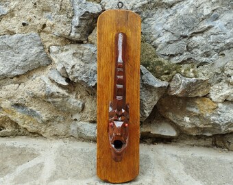 May include: A wooden wall hanging with a carved dragon head. The dragon has red eyes and an open mouth. The wood is a dark brown color.