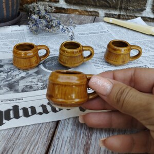 Puede incluir: Cuatro peque&ntilde;as tazas de cer&aacute;mica marr&oacute;n con forma de barril y asas. Las tazas est&aacute;n sobre un fondo de peri&oacute;dico.