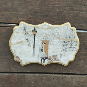 May include: A wooden plaque with a winter scene featuring a girl in a white dress standing in front of a mailbox. The scene is decorated with gold glitter and the text "Merry Xmas" is visible.