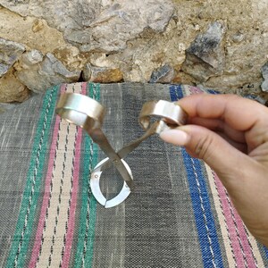 May include: A silver metal bottle opener with two circular handles. The opener is designed to be used with a twisting motion to remove bottle caps.