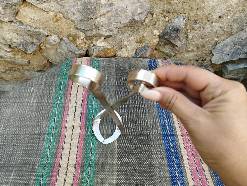 May include: A silver metal bottle opener with two circular handles. The opener is designed to be used with a twisting motion to remove bottle caps.