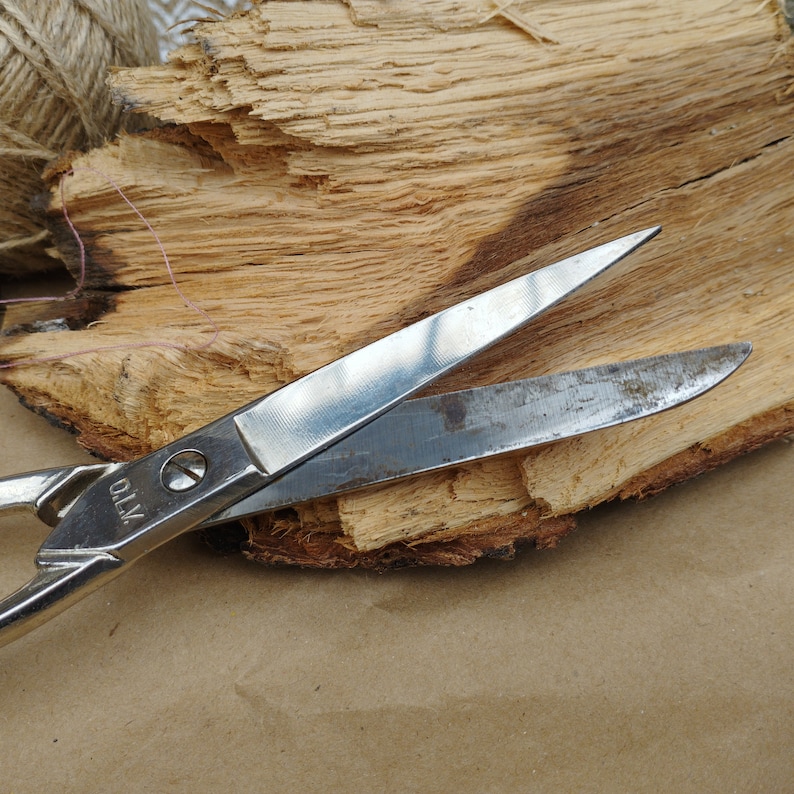 May include: A silver pair of scissors with a wooden background. The scissors have a metal handle with the word "X70" printed on it.