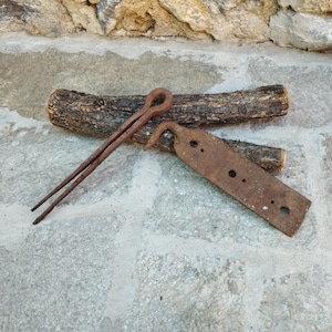 May include: Two rusty metal tools, one with a hook and the other with a long, thin handle, are lying on a piece of wood.