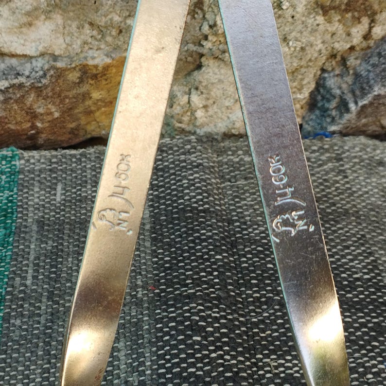 May include: Two gold-colored metal measuring tools with the text "H-50X" and "H-60X" engraved on them.